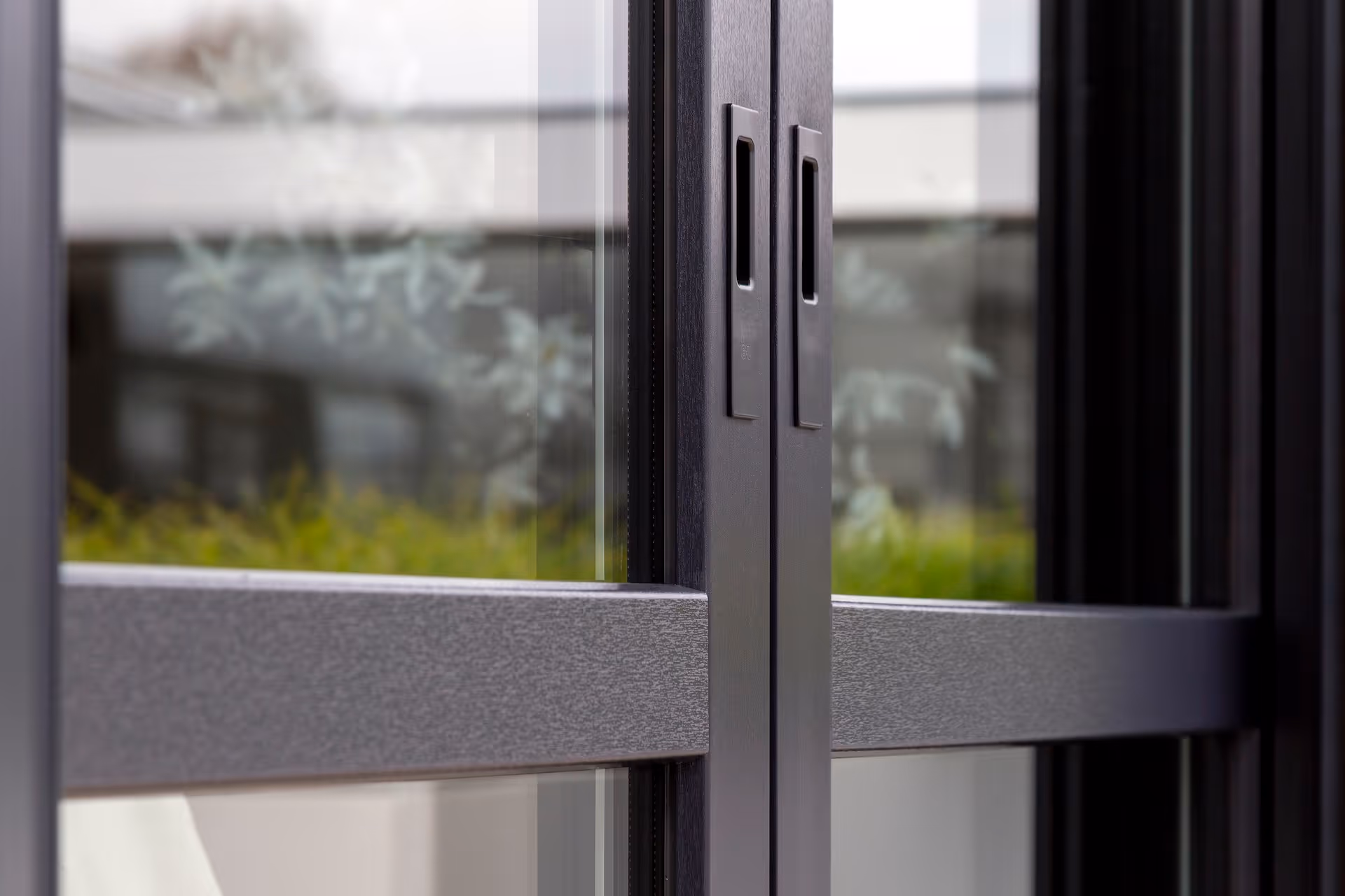 Detail van zwarte metalen schuifdeuren met glazen panelen en geïntegreerde handgrepen.