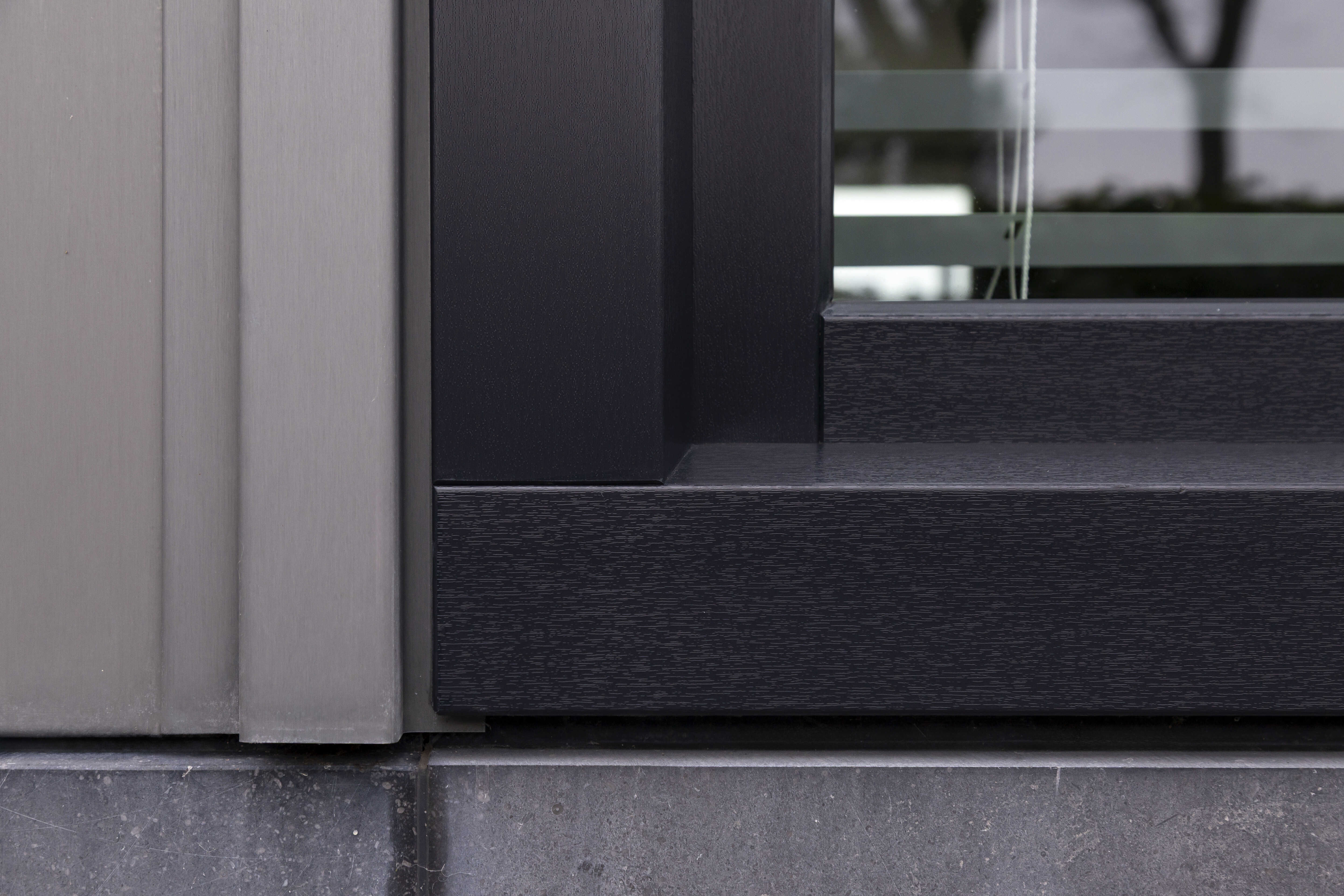 Close-up van een moderne raamstijl met zwarte houten en grijze metalen elementen op een stenen vensterbank.