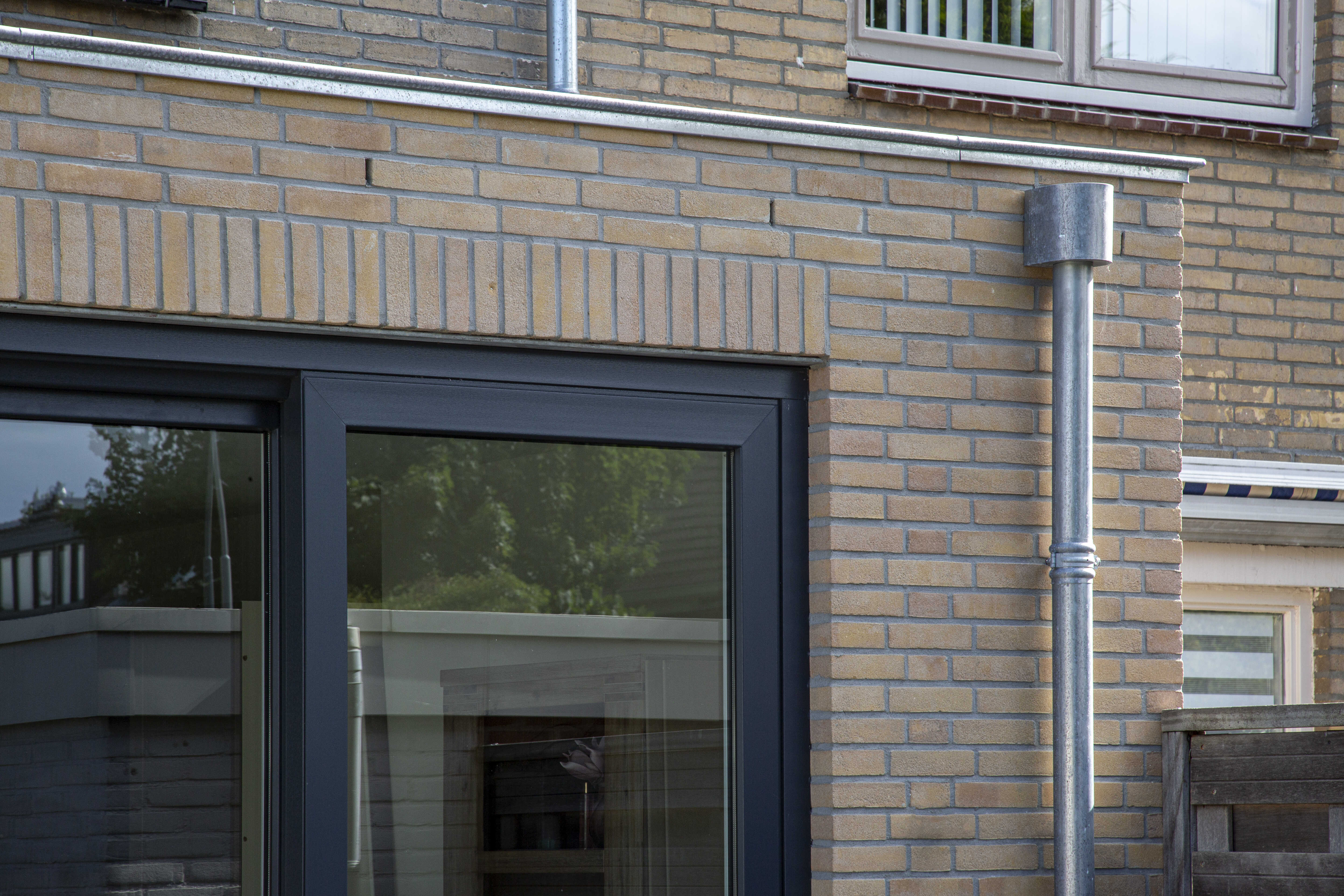 Bakstenen buitenmuur met een zwarte deur en een metalen regenpijp.