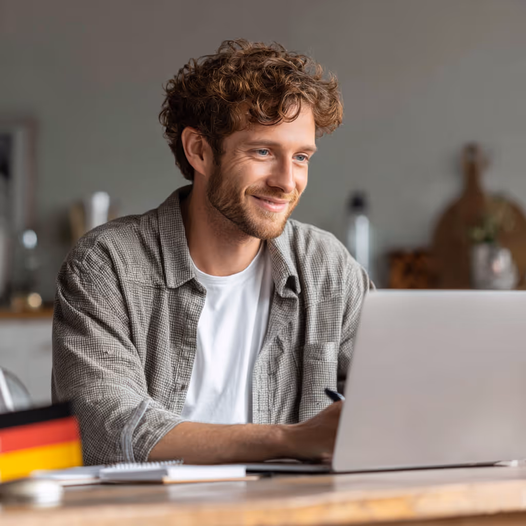 Two smiling women wearing sunglasses and floral dresses sitting at an outdoor cafe with historic buildings in the background.
