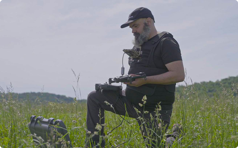 Man kneeling in a meadow while operating a drone
