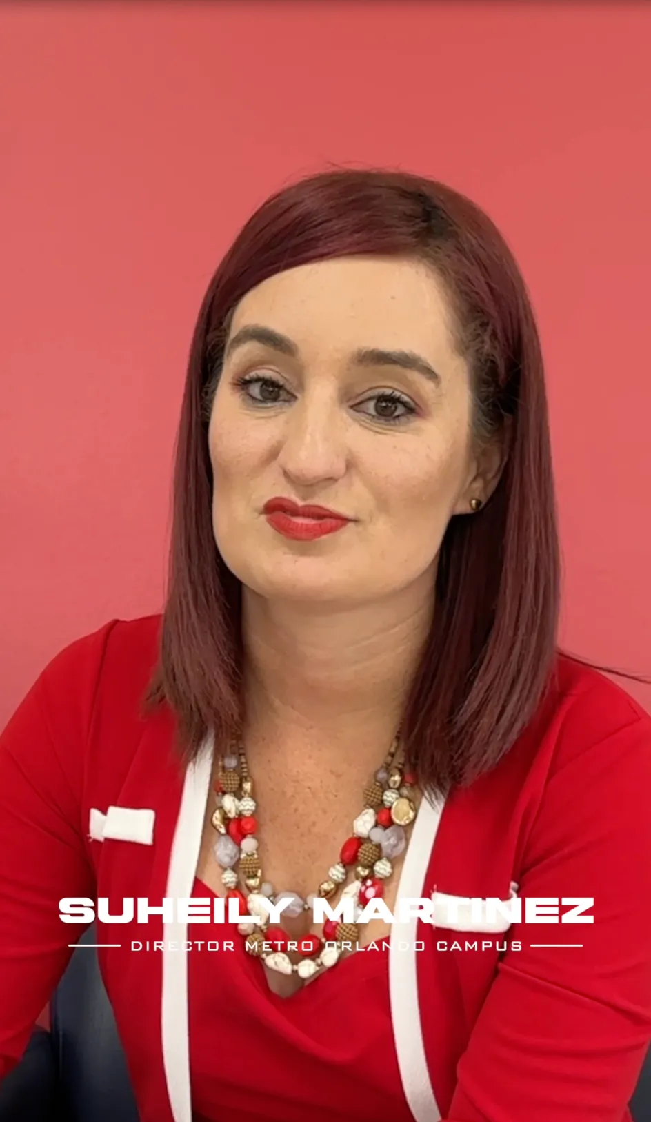 Portrait of Suheily Martinez wearing a red top and multicolored beaded necklace against a red background.