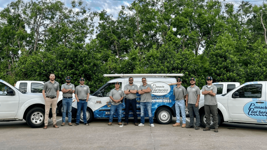 Eight men in gray polos standing in front of vans and trucks branded with Pinnacle Pool Service logos and contact information, set against a backdrop of green trees.