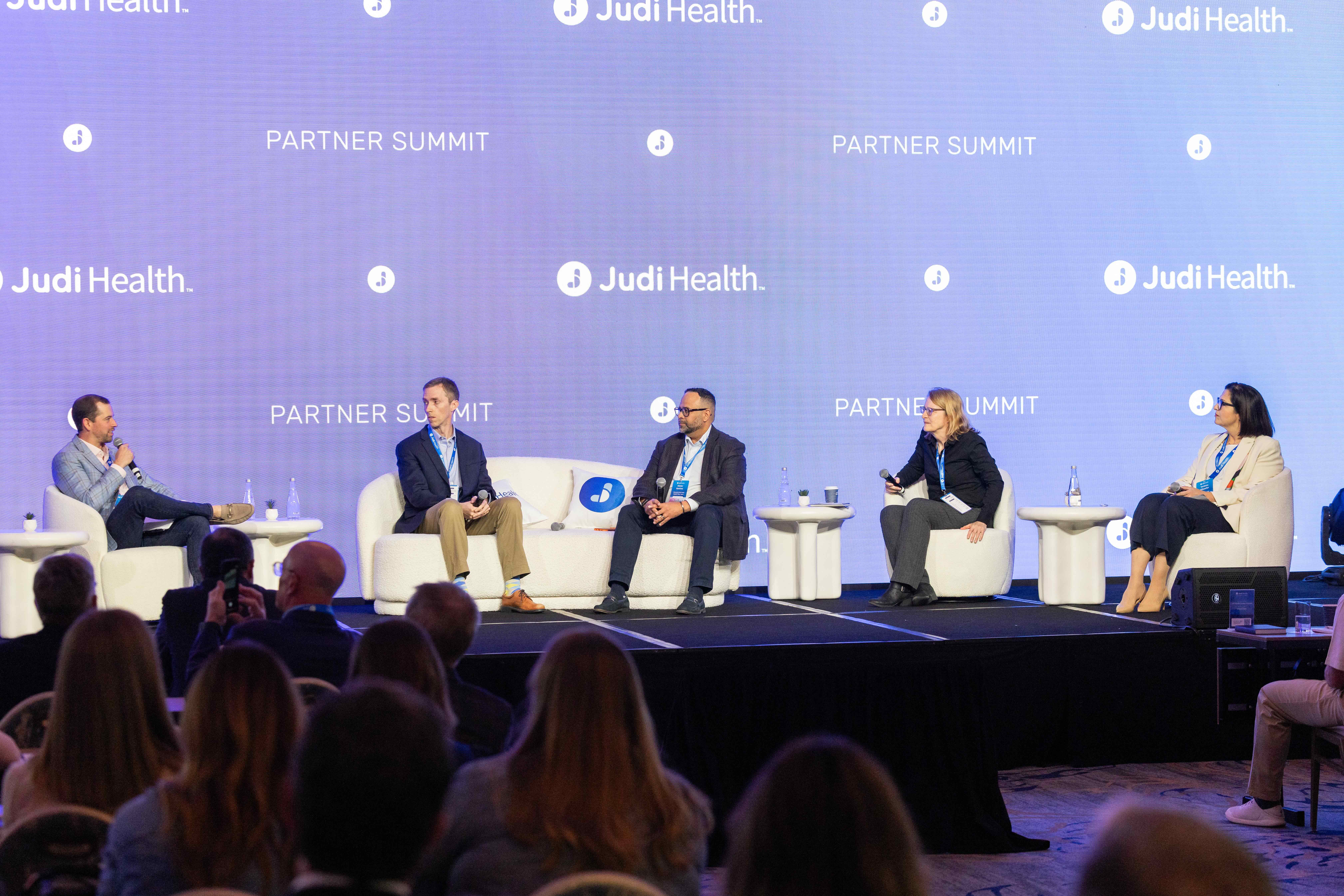 Five speakers on stage at the Judi Health Partner Summit, discussing various topics.