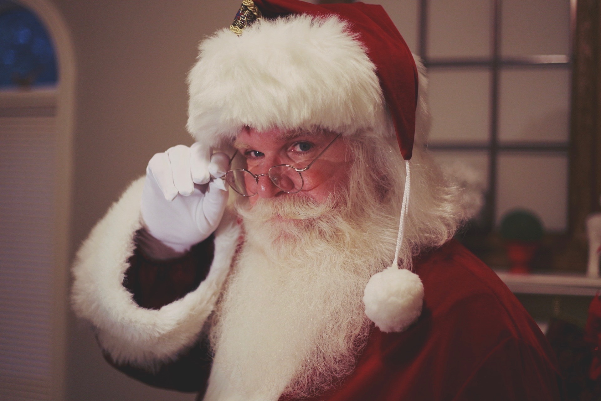 Close-up of a smiling Santa Claus wearing a red hat, glasses, and a fluffy white beard.