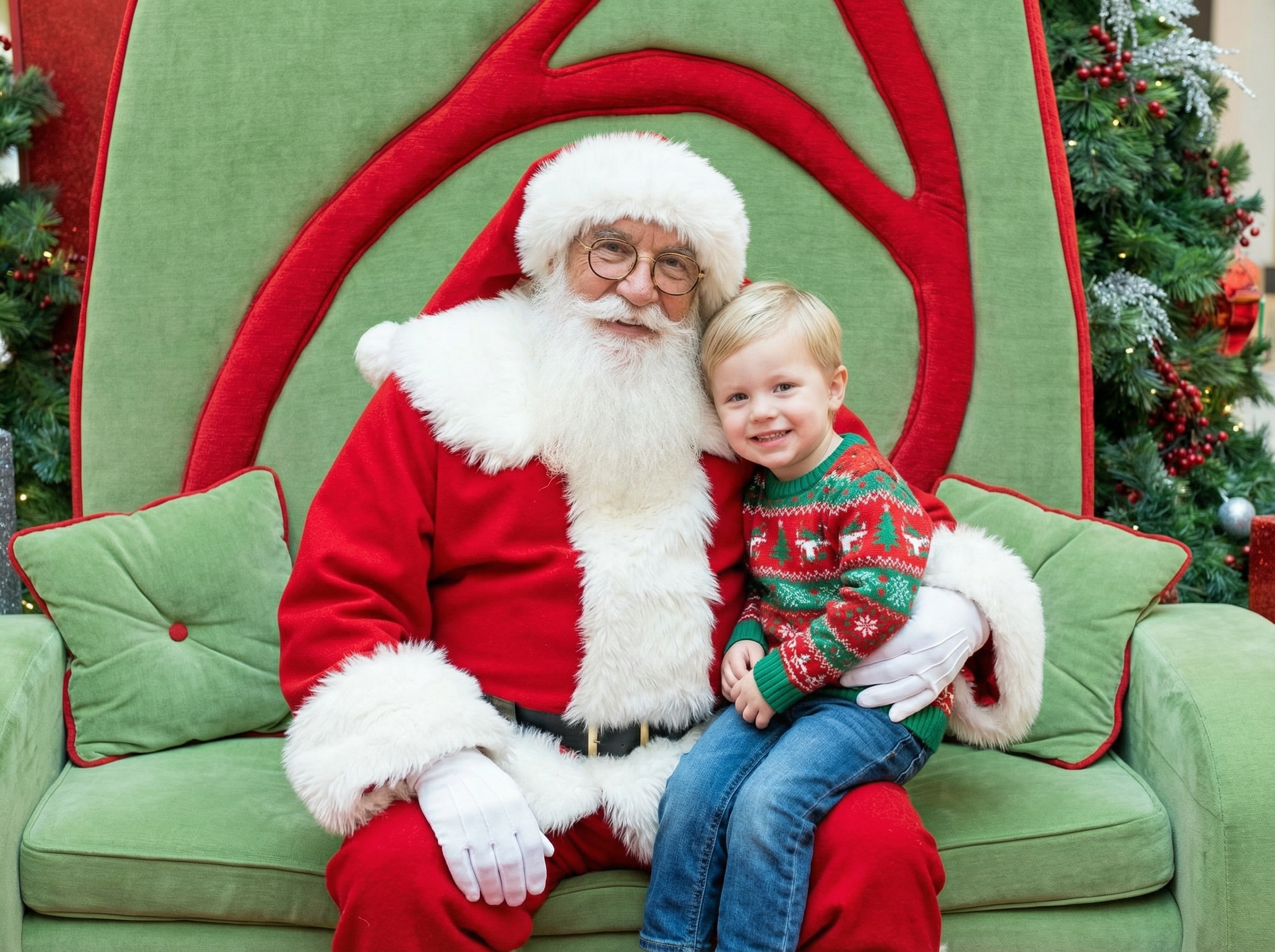 Santa Claus sitting between a smiling little girl holding a 'Nice' sign and a boy making a scrunched face on a green couch.