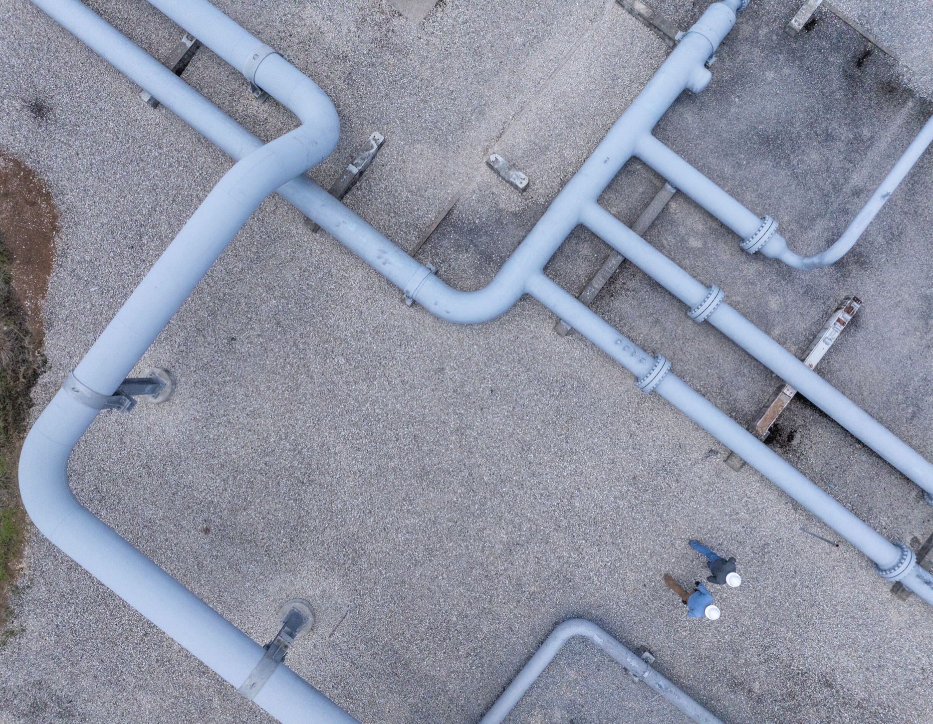 A happy Boardwalk employee wearing a white hardhat, holding a clipboard, and standing in front of pipeline equipment