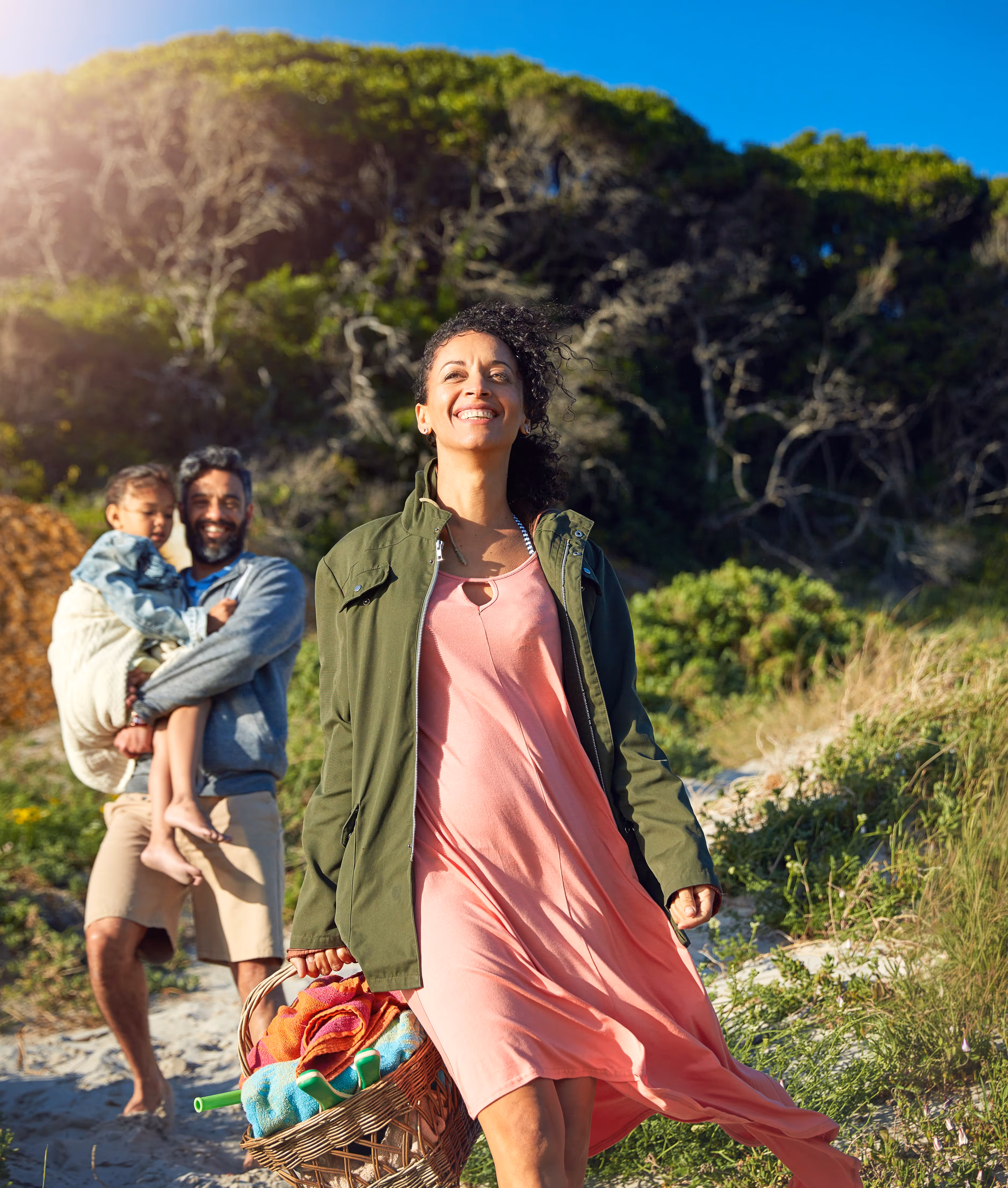 A woman happily looks up, her husband and child look at her also looking happy, they seem to walk near a beach.