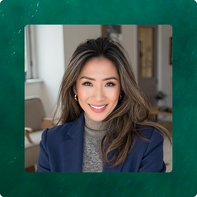 Smiling woman with long hair, wearing a navy blazer and gray turtleneck sweater, sitting indoors.