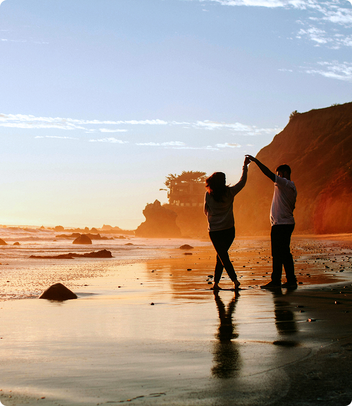 Silhouette of a couple dancing on a beach at sunset with cliffs and ocean in the background.