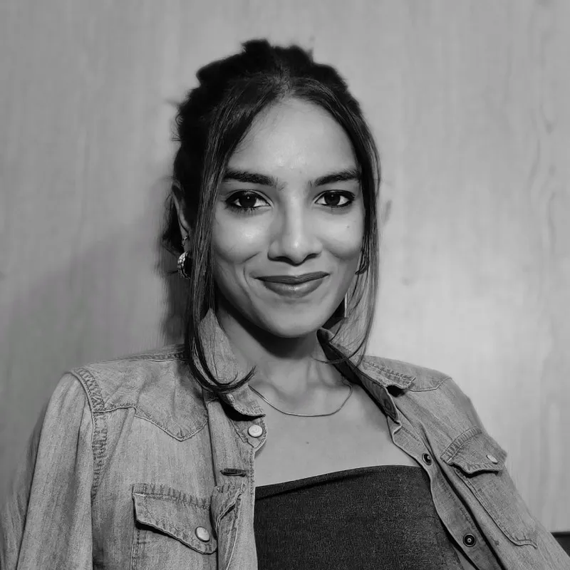 Smiling woman with dark hair in a denim jacket and strapless top against a plain background.