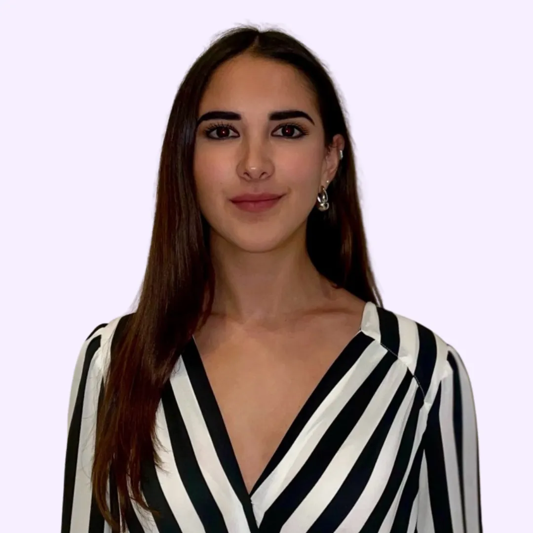 Portrait of a woman with long brown hair wearing a black and white striped blouse and silver hoop earrings, against a light purple background.