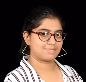 Woman with long dark hair wearing large glasses, a black jacket, pearl necklace, and decorative earrings, smiling and touching her glasses.