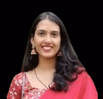 Woman with long dark hair wearing large glasses, a black jacket, pearl necklace, and decorative earrings, smiling and touching her glasses.