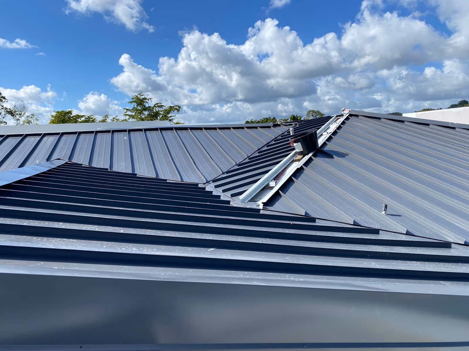 Blue metal roof with clear ribs under a partly cloudy sky.