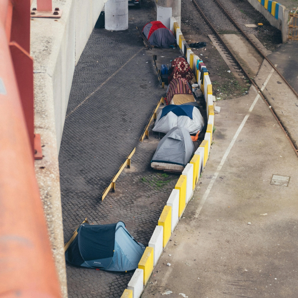 Several tents from a homeless encampment are pictured underneath a bridge in a non-descript city.