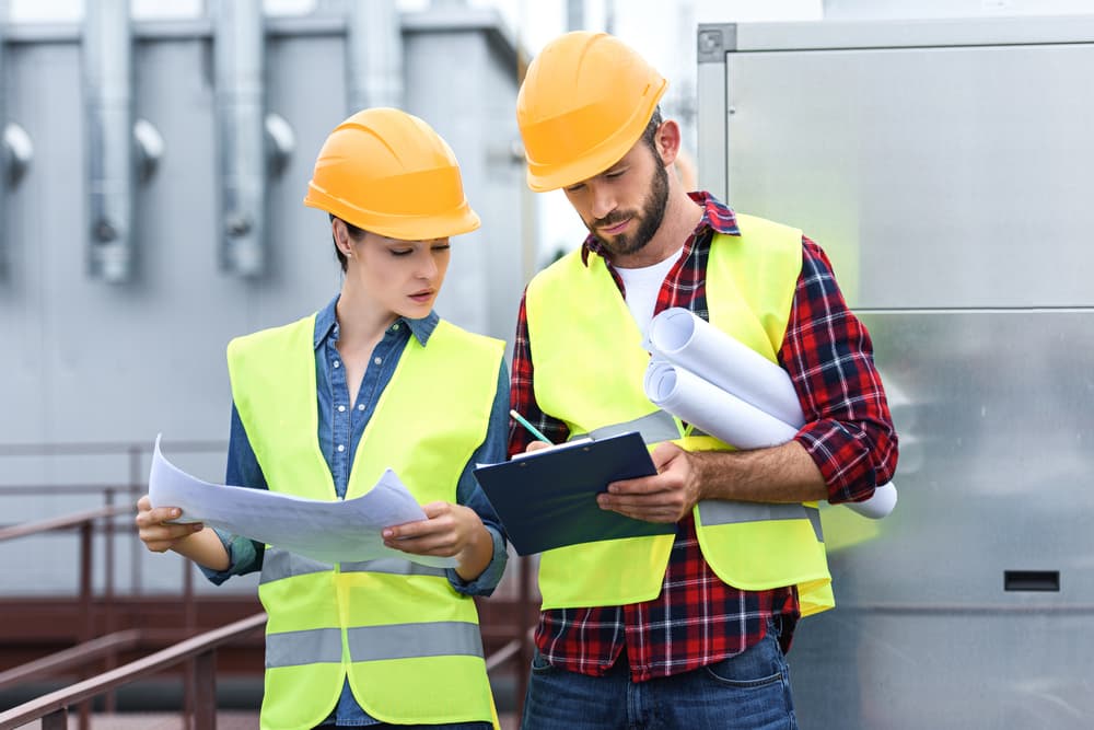 Two contractors in hard hats reviewing construction plans and notes on-site, symbolizing professional liability insurance for builders and service professionals.
