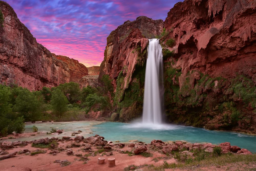 Scenic view of Havasu Falls in Havasupai, Arizona, with red canyon cliffs and turquoise water at sunset.