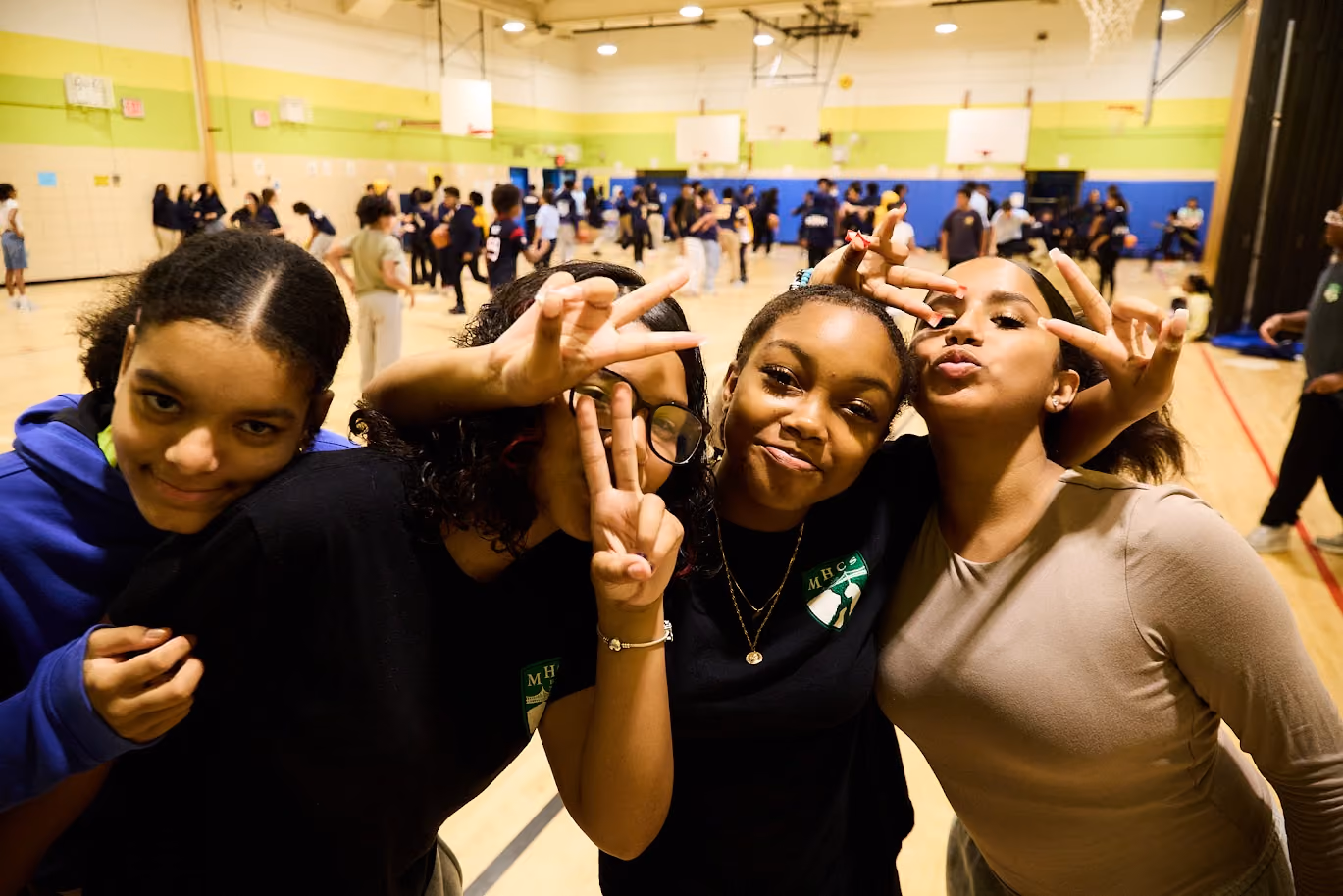 Four students posing and smiling together in school gymnasium