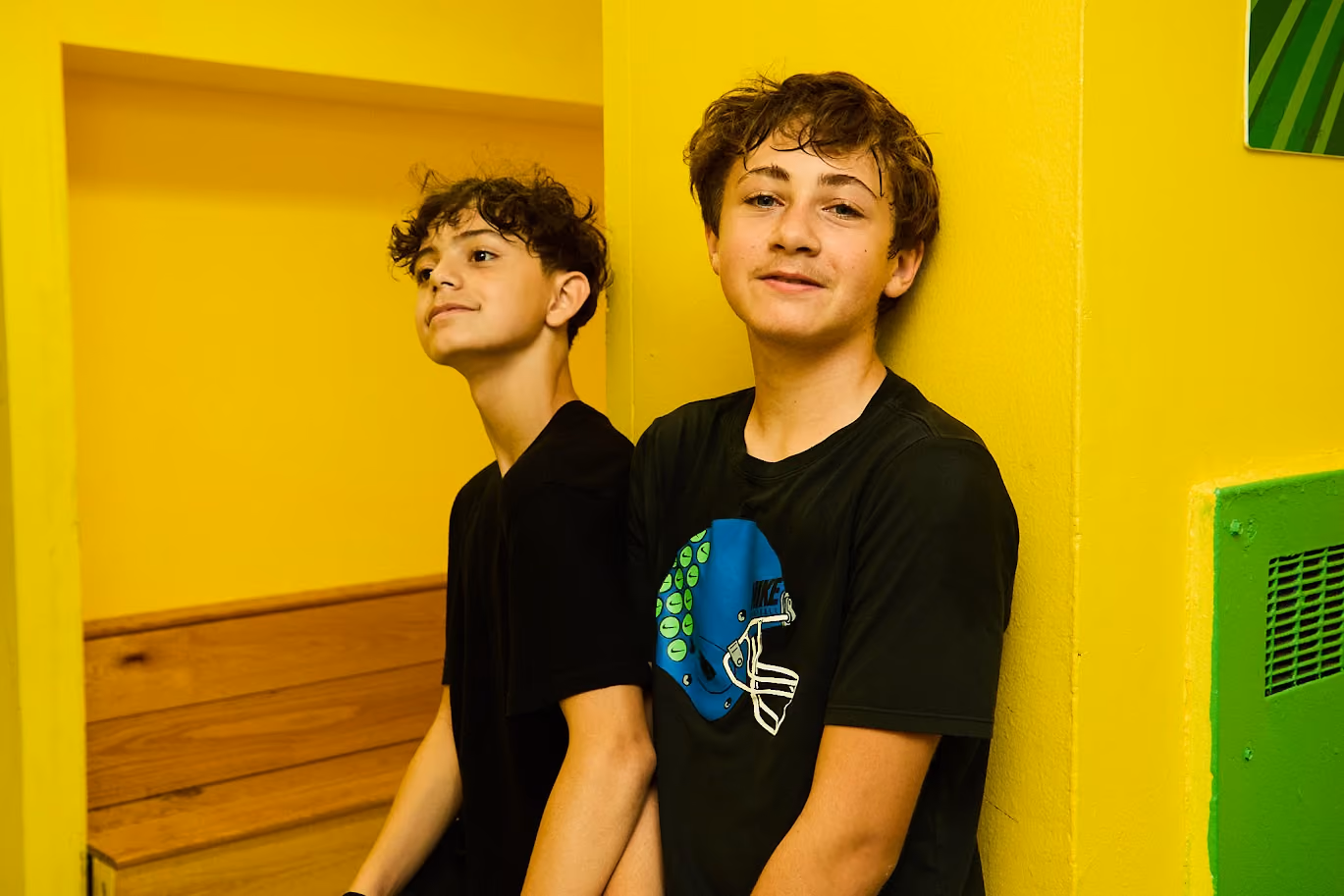 Two middle school students smiling against a bright yellow wall