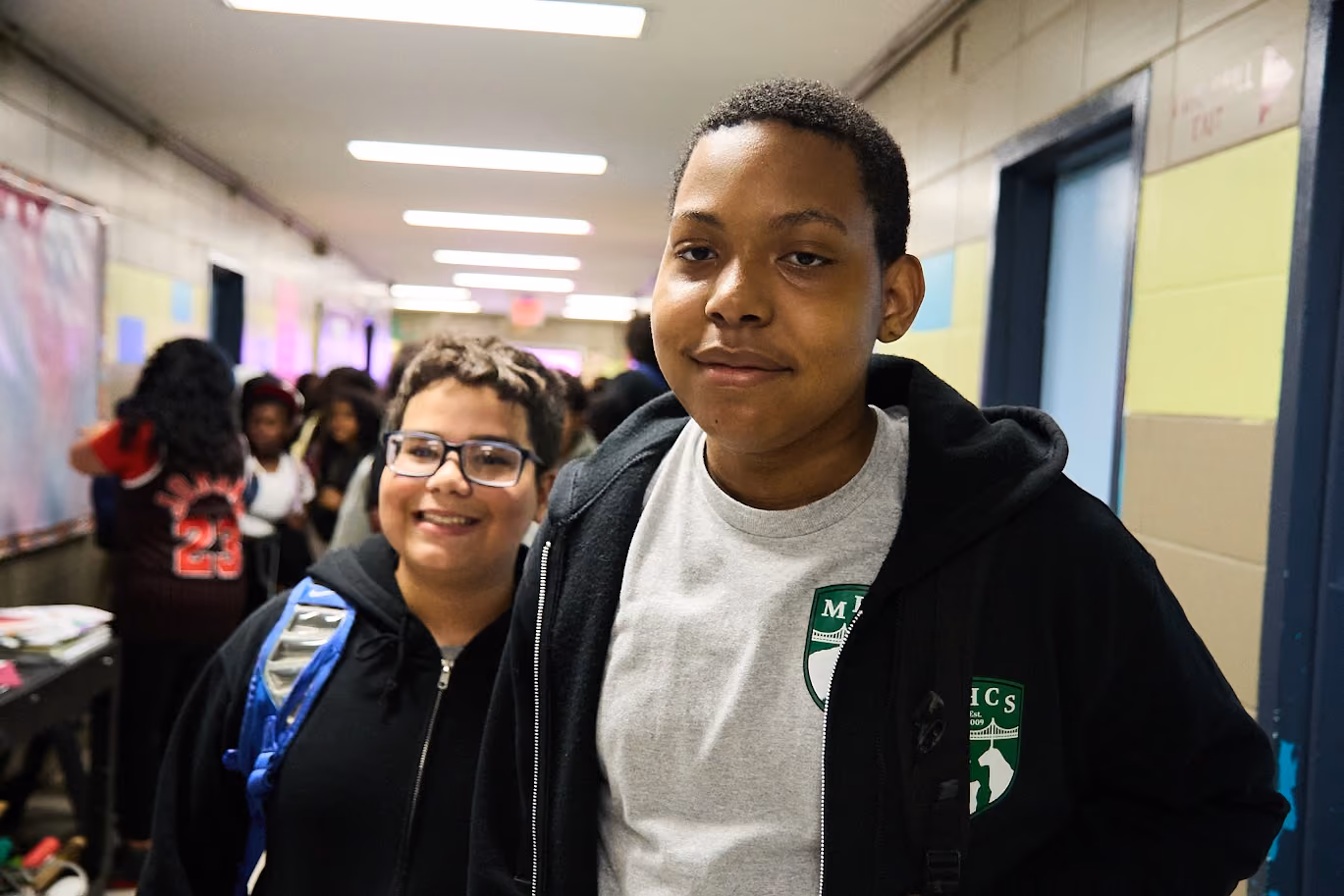 Two smiling middle school students standing together in a school hallway