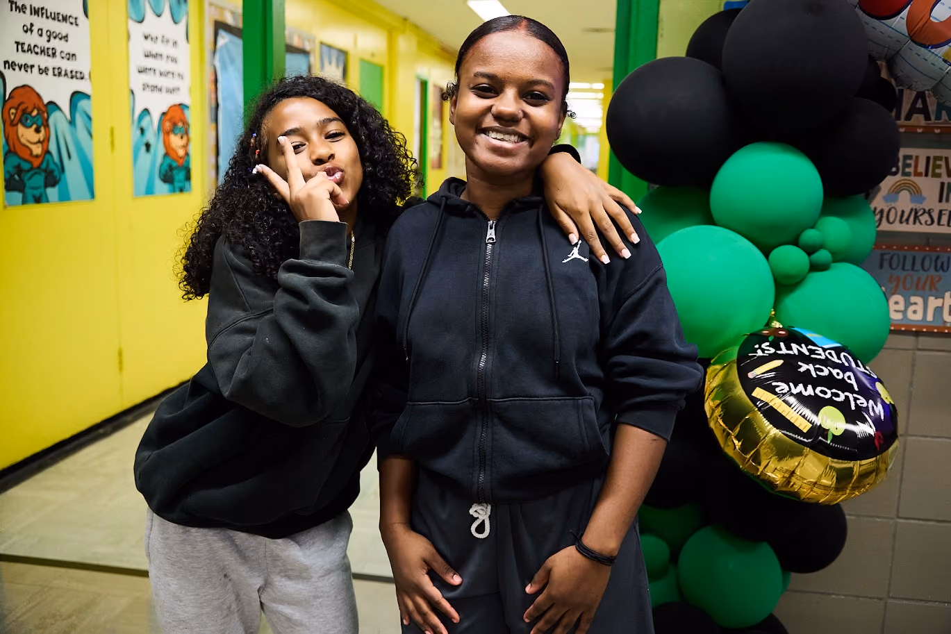 Two students posing together near welcome back balloons in school hallway