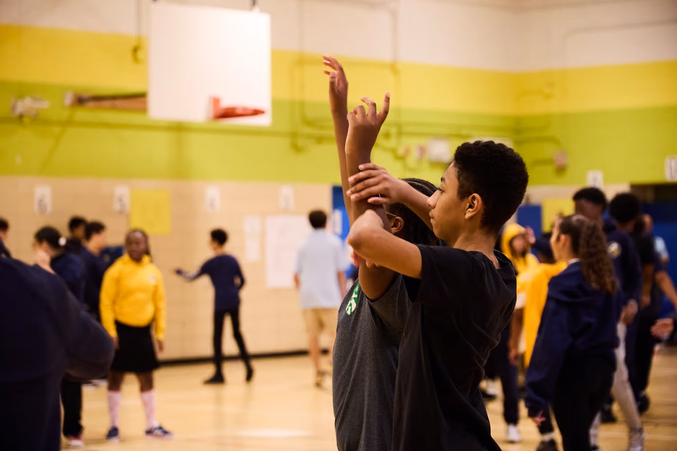 Students practicing basketball skills in school gymnasium during physical education class