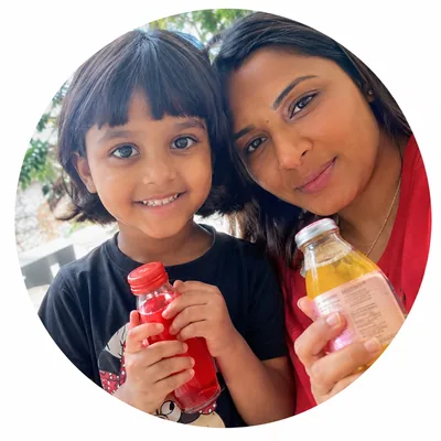 Woman and young girl smiling and holding bottles of red and yellow drinks outdoors.