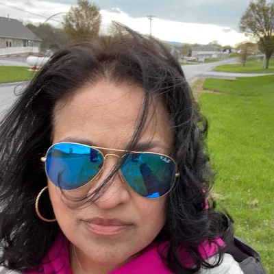 Woman with dark hair wearing blue reflective sunglasses and gold hoop earrings outdoors.
