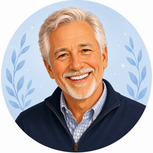 Smiling older man with white hair and beard wearing a blue jacket and checkered shirt on a light blue background.