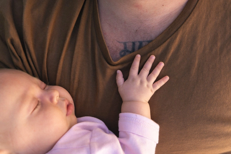 A newborn baby holding her hand at her fathers chest 