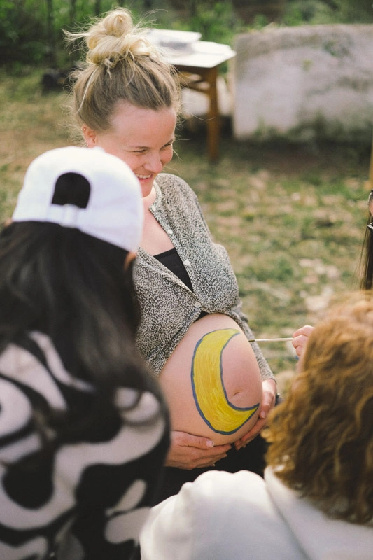 Women painting a pregnant woman's belly on a babyshower 