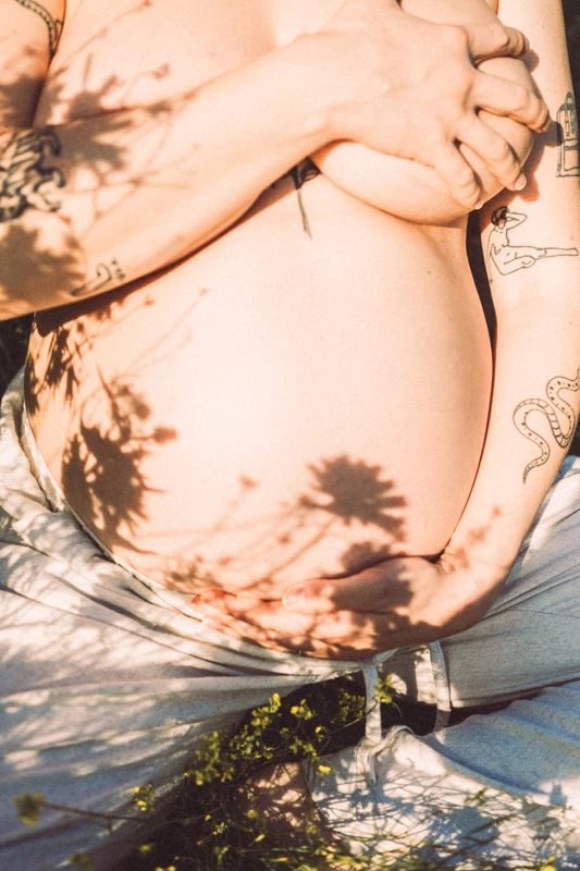 A naked pregnant women sitting in the grass holding her belly
