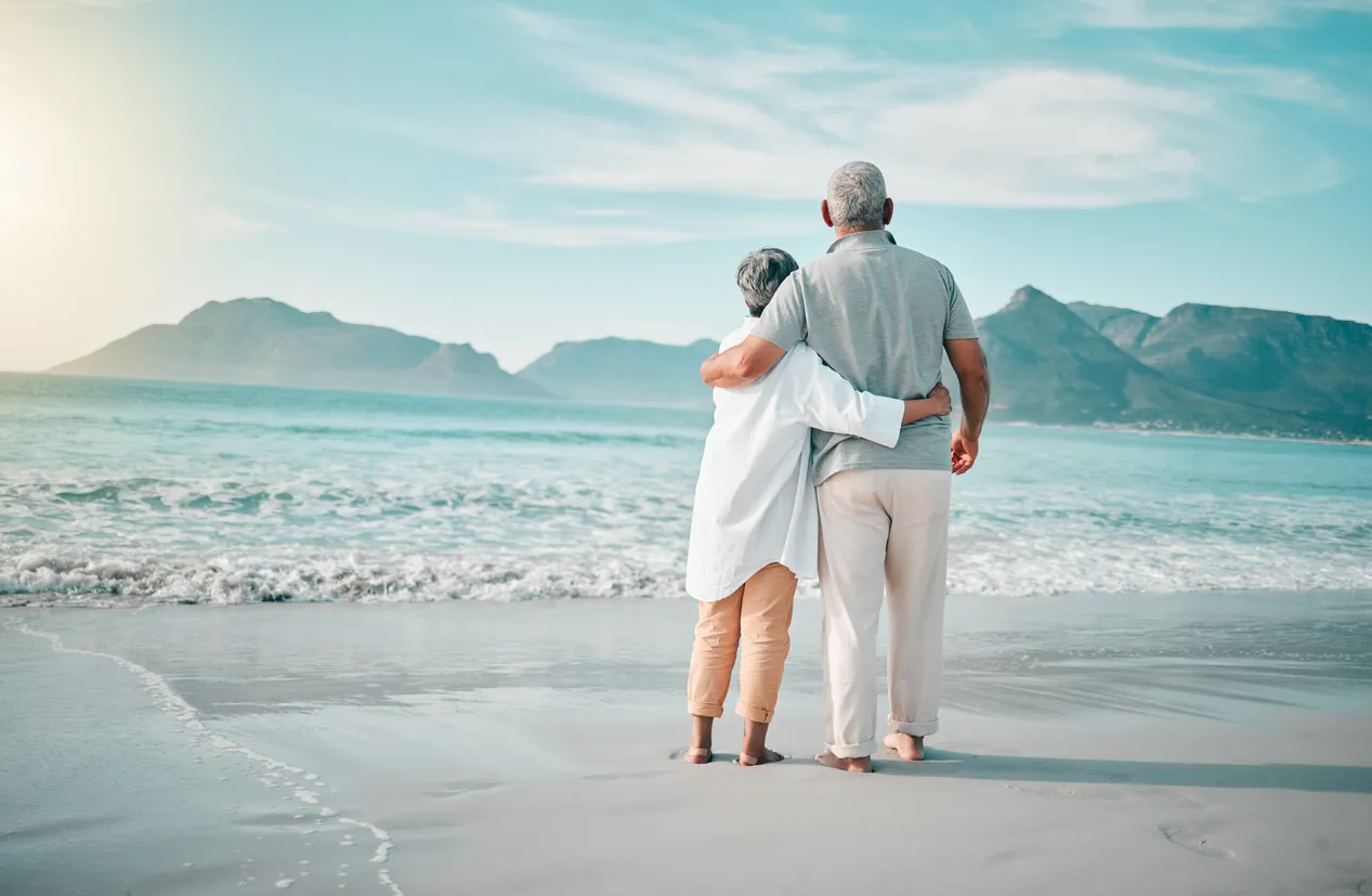 Elderly couple embracing on a beach while looking out at the ocean