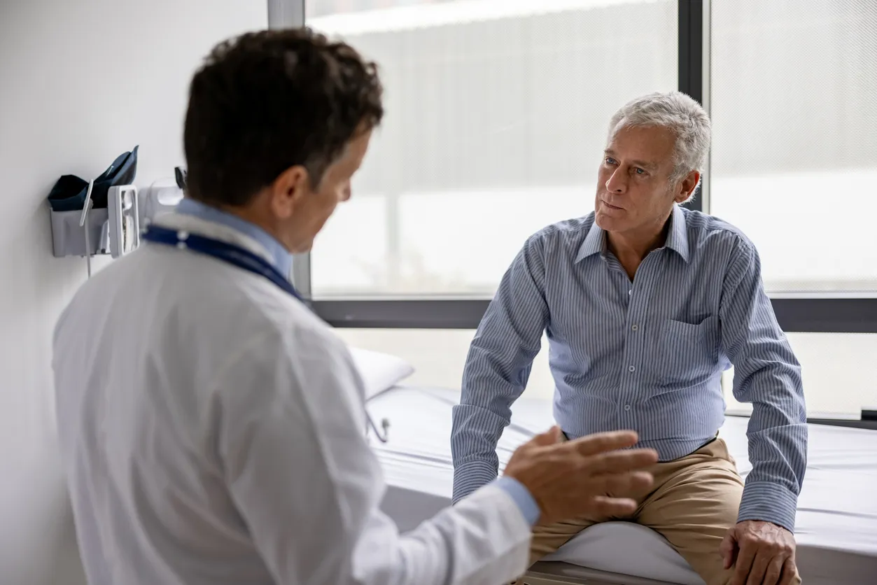 Older man in a striped shirt talking with a doctor in a white coat during a visit