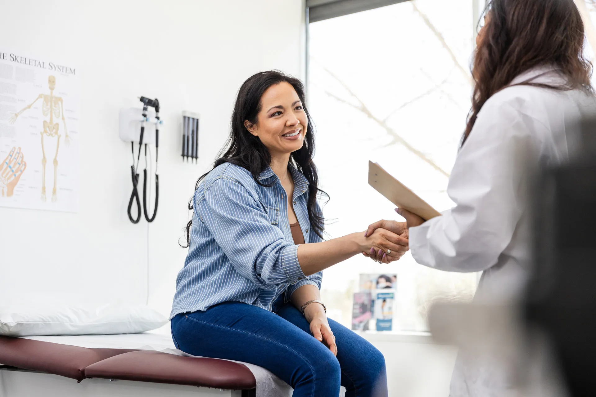 Woman on a medical exam table shaking hands with a doctor in a bright clinic