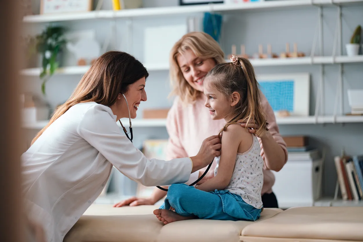 Doctor using a stethoscope to examine a young girl while her mother watches