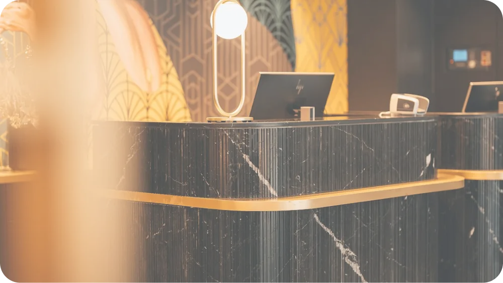 Modern reception desk with black marble finish and gold trim, featuring a computer monitor and a stylish lamp.