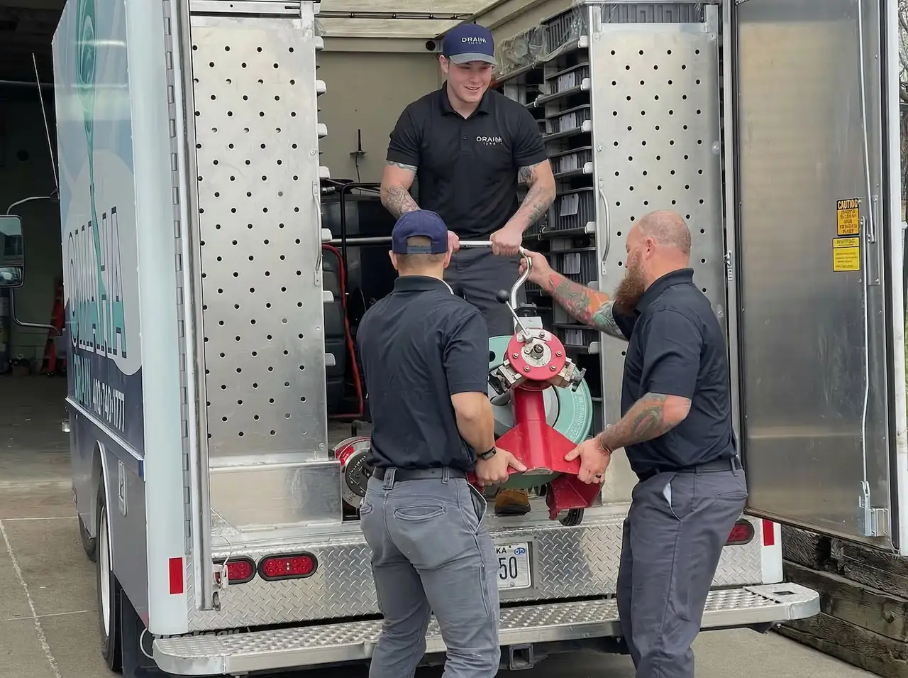 Omaha Drain technicians loading drain cleaning equipment from a service truck