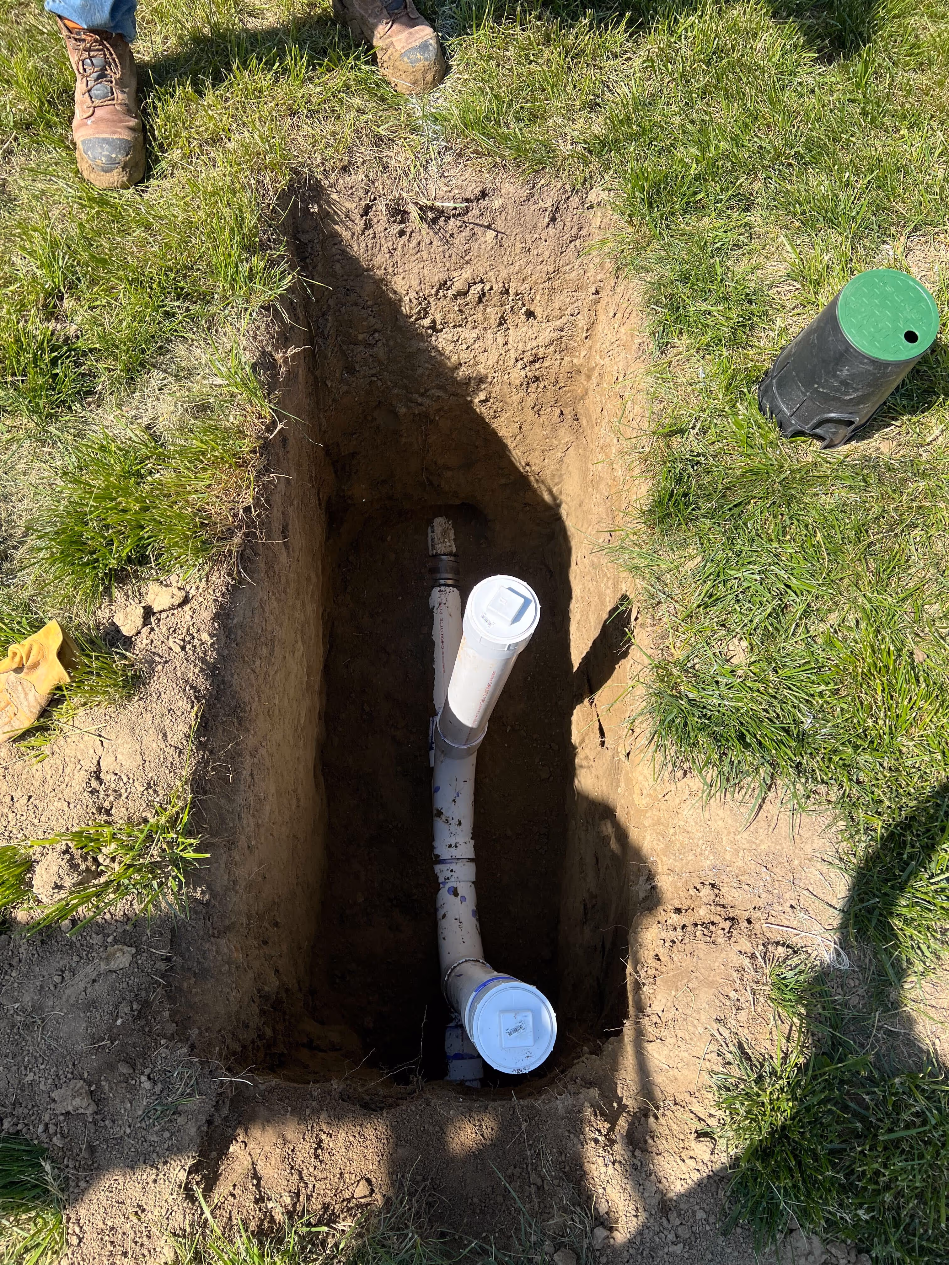 Two-way sewer cleanout with white PVC caps installed in a dug hole in a front lawn
