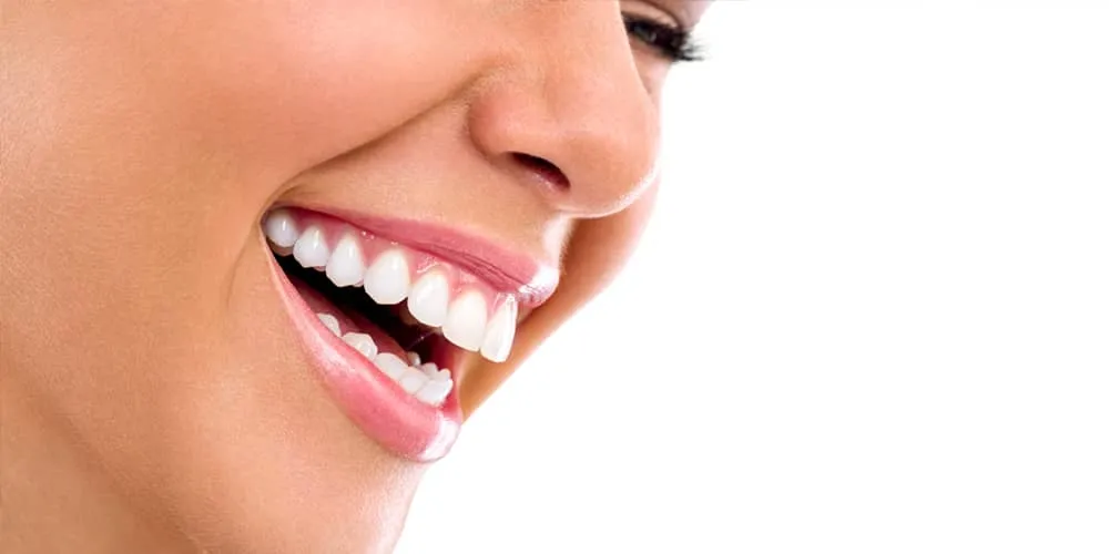Close-up of a smiling person's face showing white teeth and pink lips against a white background.
