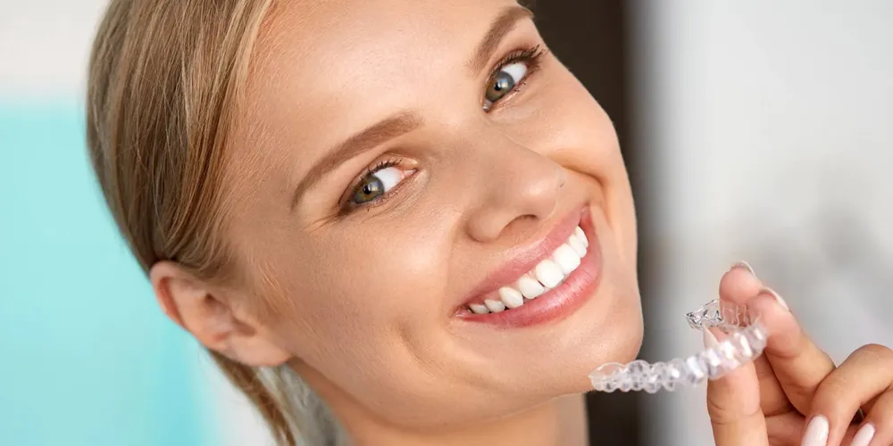 Smiling woman holding a clear dental aligner near her teeth.