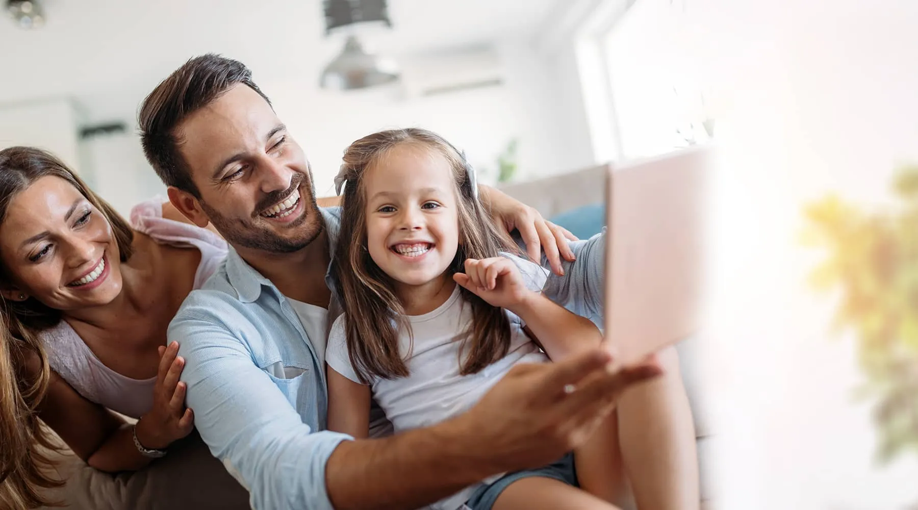 Smiling parents taking a selfie with their daughter at home.