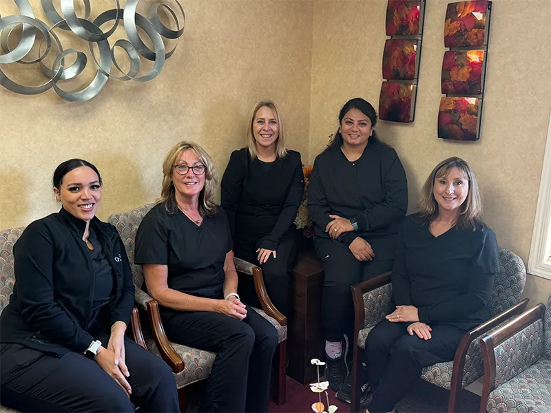 Group of five women sitting and smiling in a cozy room with beige walls and modern decor.