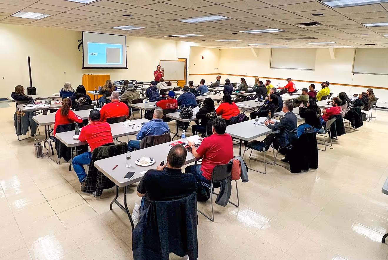 A large group of people attentively listens to a speaker during a training session in a classroom setting.