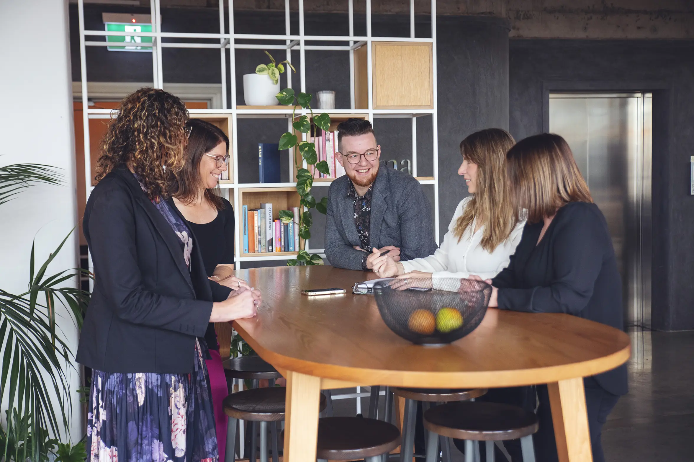Team of lawyers smiling and sitting in an office discussing legal support for businesses, property and employers surrounded by books and plants
