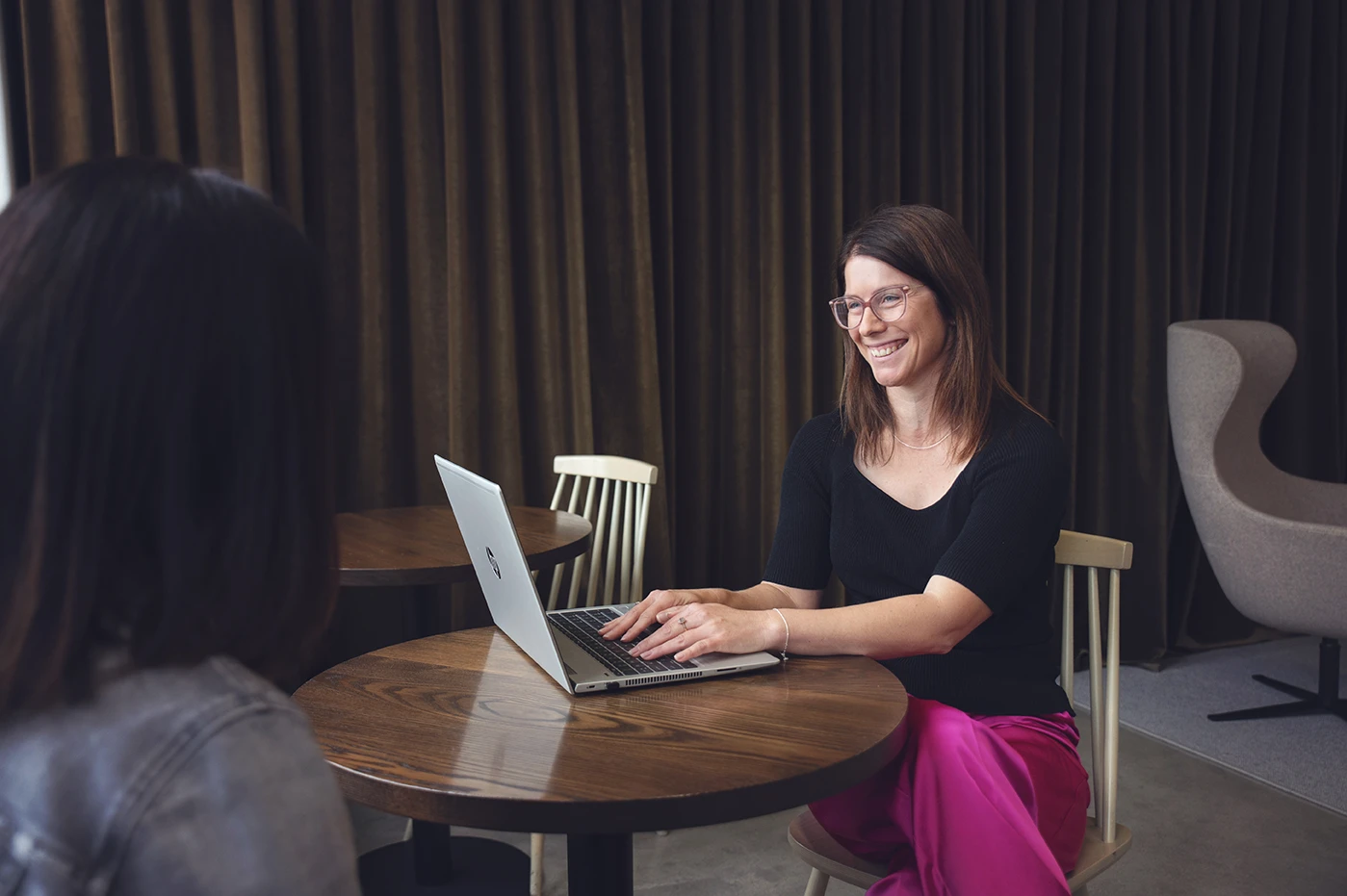 A smiling woman doing legal consultation with a client, sitting at a round table with a laptop