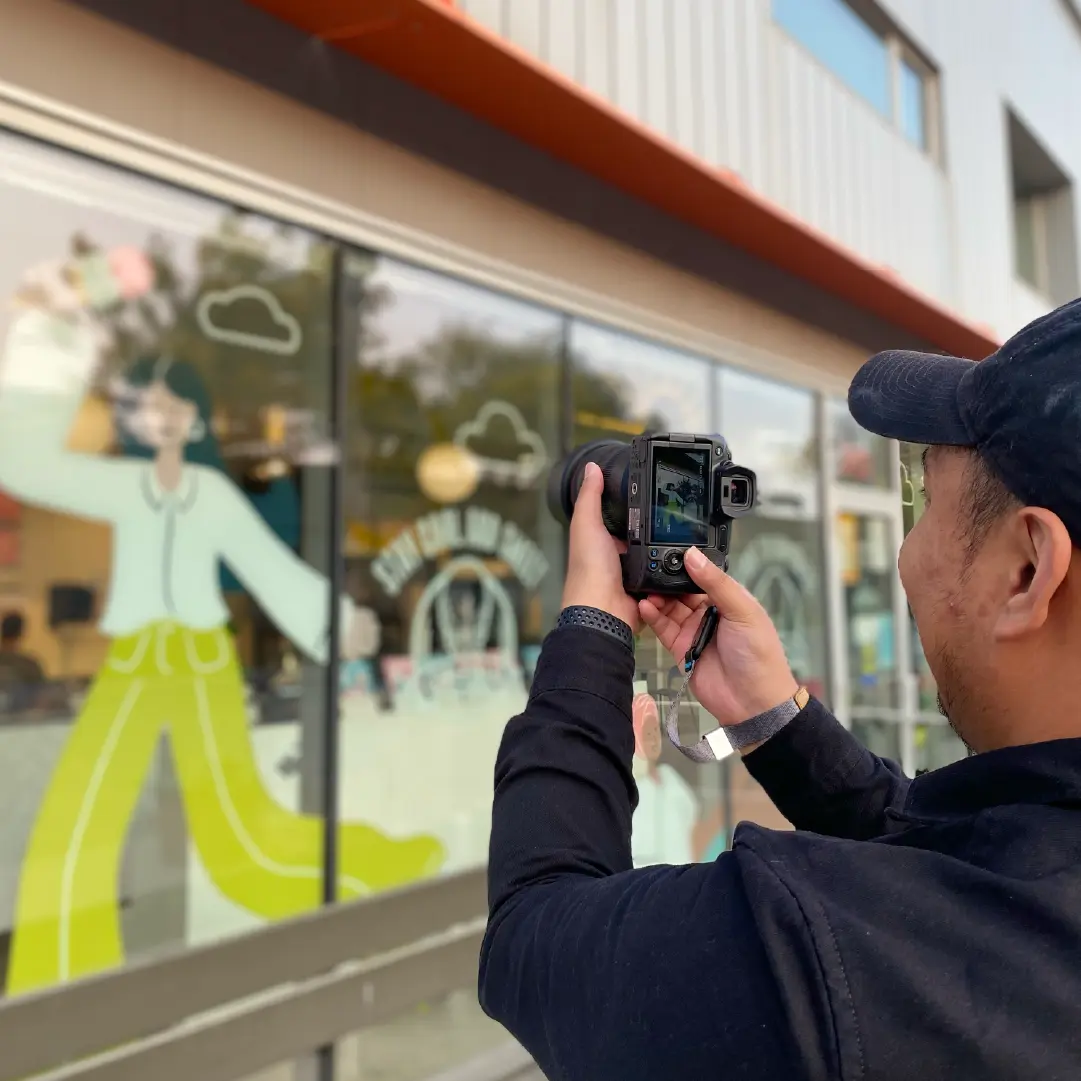 Photographer capturing branded storefront window graphics, representing brand rollout, environmental branding, and real-world implementation.