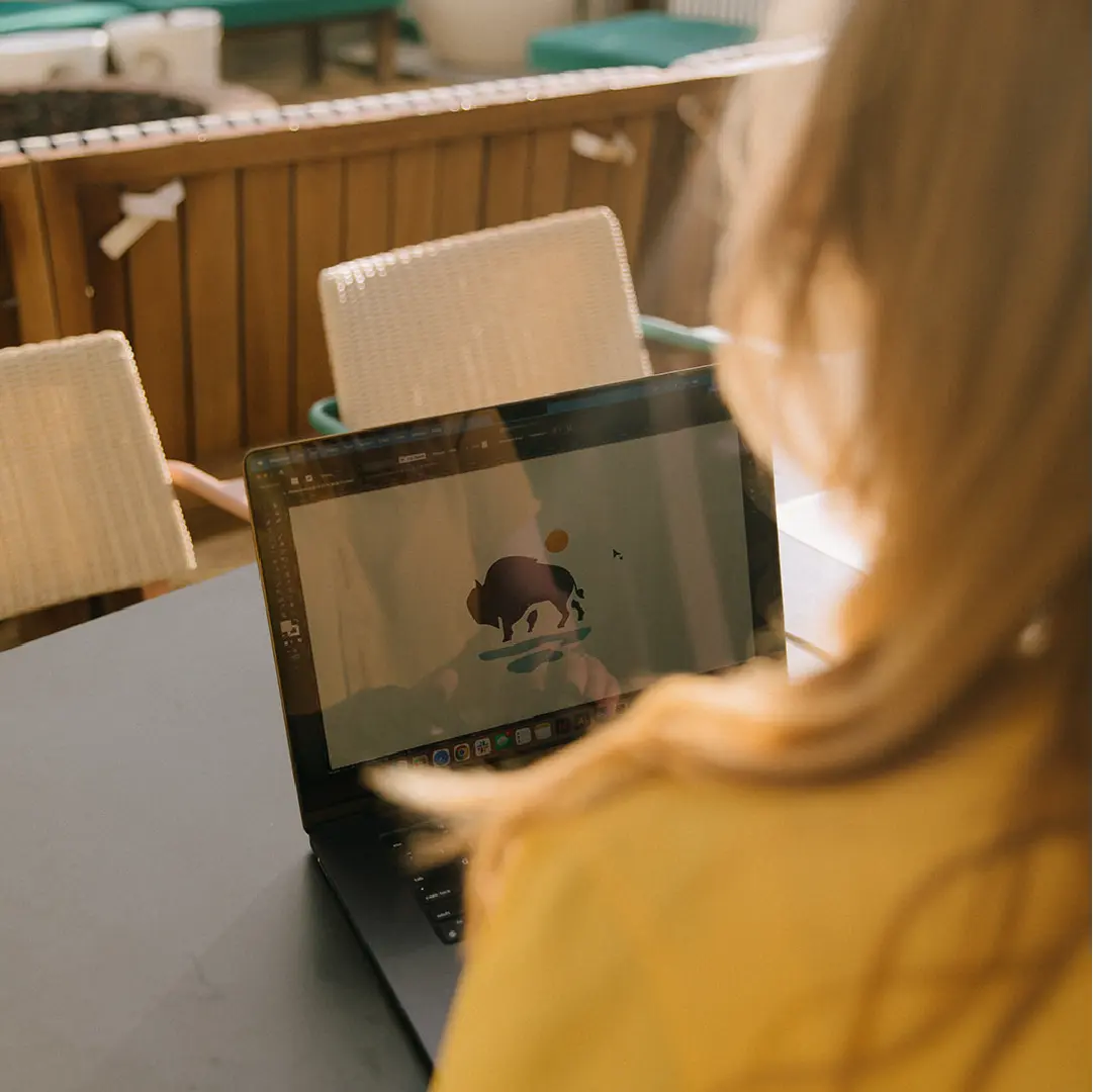 Over-the-shoulder view of a designer refining a logo on a laptop, showing the hands-on creative process behind brand identity development.