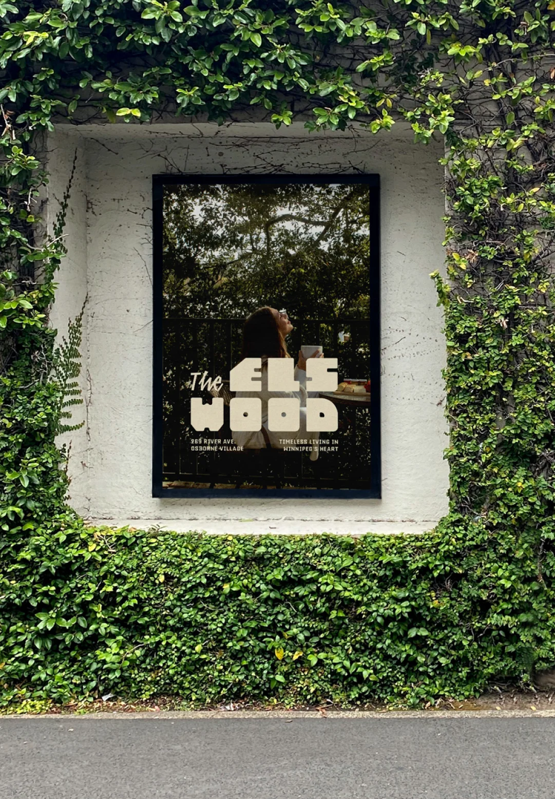 Framed branded poster displayed in a vine-covered exterior wall, showing environmental branding and place-based marketing for a hospitality or lifestyle destination.
